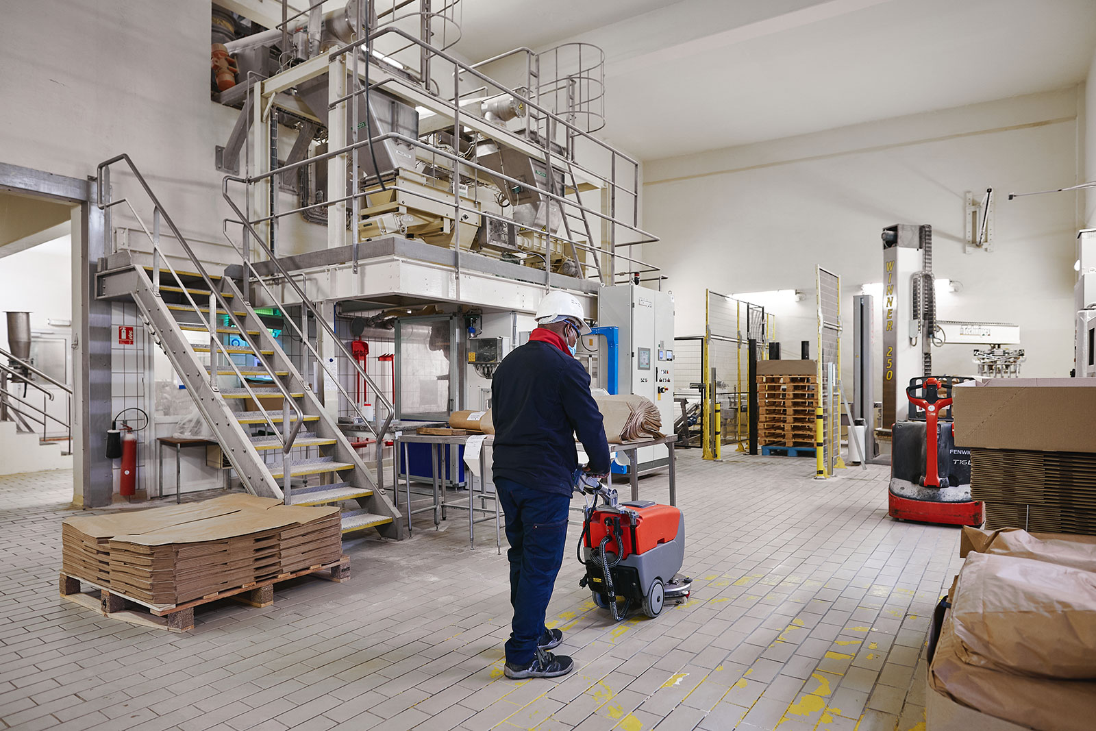Homme nettoyant le sol d'une entreprise du secteur de l'industrie lourde avec une machine professionnelle.